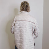 Person wearing a quilted jacket against a plain wall