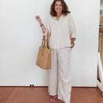Woman in a white outfit holding a beige handbag against a white wall.