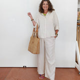 Woman in a white outfit holding a beige handbag against a white wall.