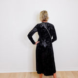 Person wearing a black floral velvet dress against a white wall.