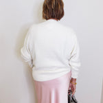 woman wearing a cream sweater against a white background. 