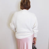 woman wearing a cream sweater against a white background. 