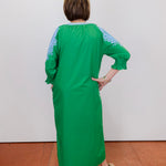 Person wearing a green dress with blue patterns on a white wall.