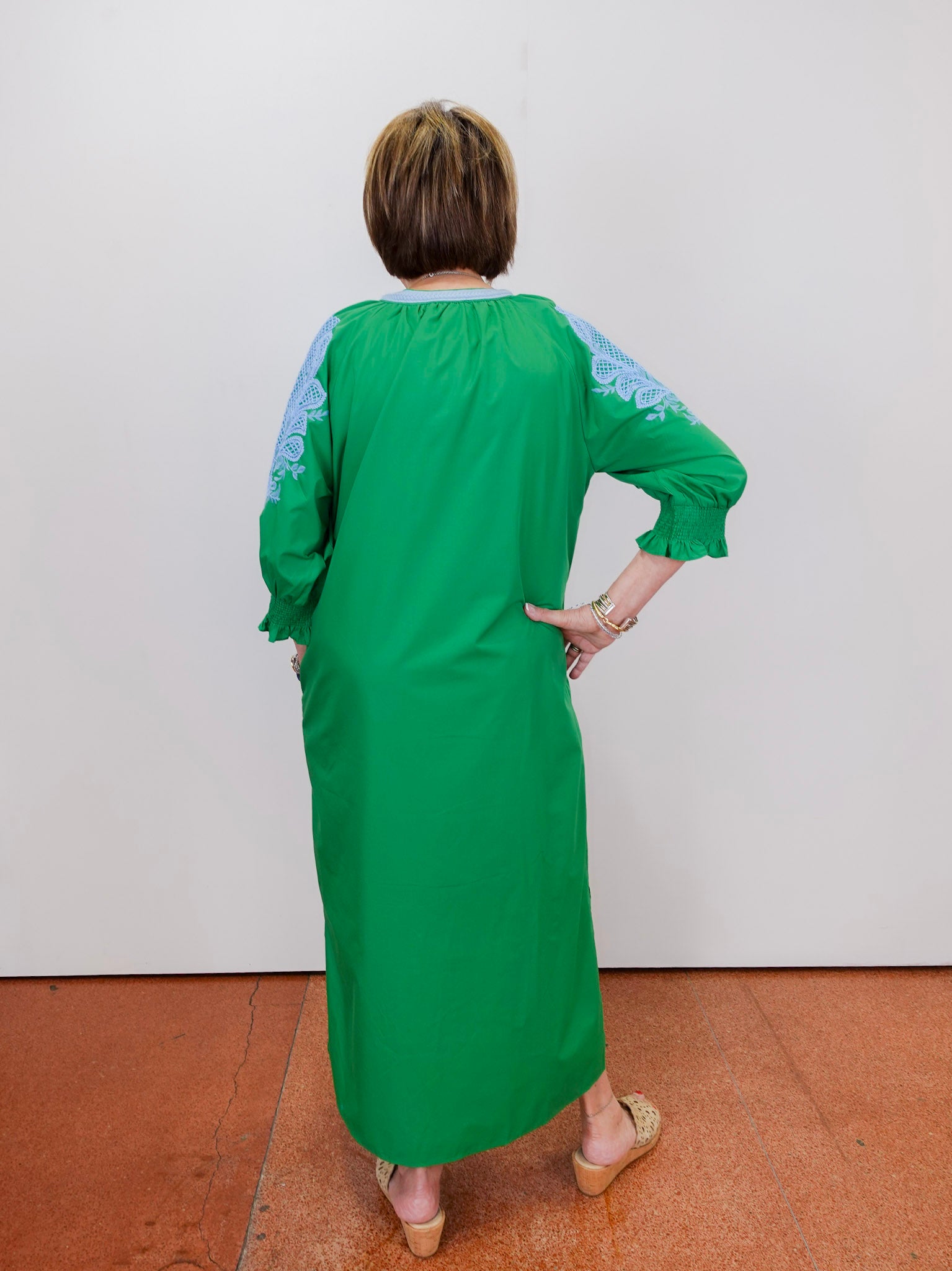 Person wearing a green dress with blue patterns on a white wall.