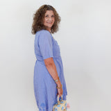 Woman wearing a light blue dress holding a floral handbag against a white background