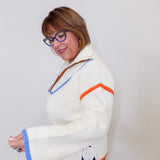 Woman wearing a white sweater with colorful accents against a plain background