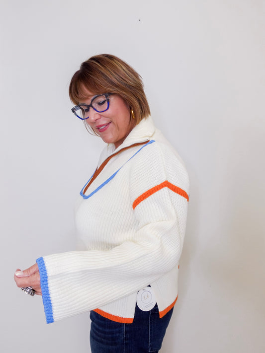 Woman wearing a white sweater with colorful accents against a plain background