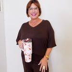 Woman in brown outfit holding a floral-patterned mug against a white wall