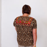 Person wearing a leopard print top with colorful embroidery against a white wall