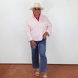 Person wearing a red and white striped shirt, blue jeans, and a beige hat against a white wall.