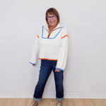 Person wearing a colorful sweater and jeans standing against a white wall.