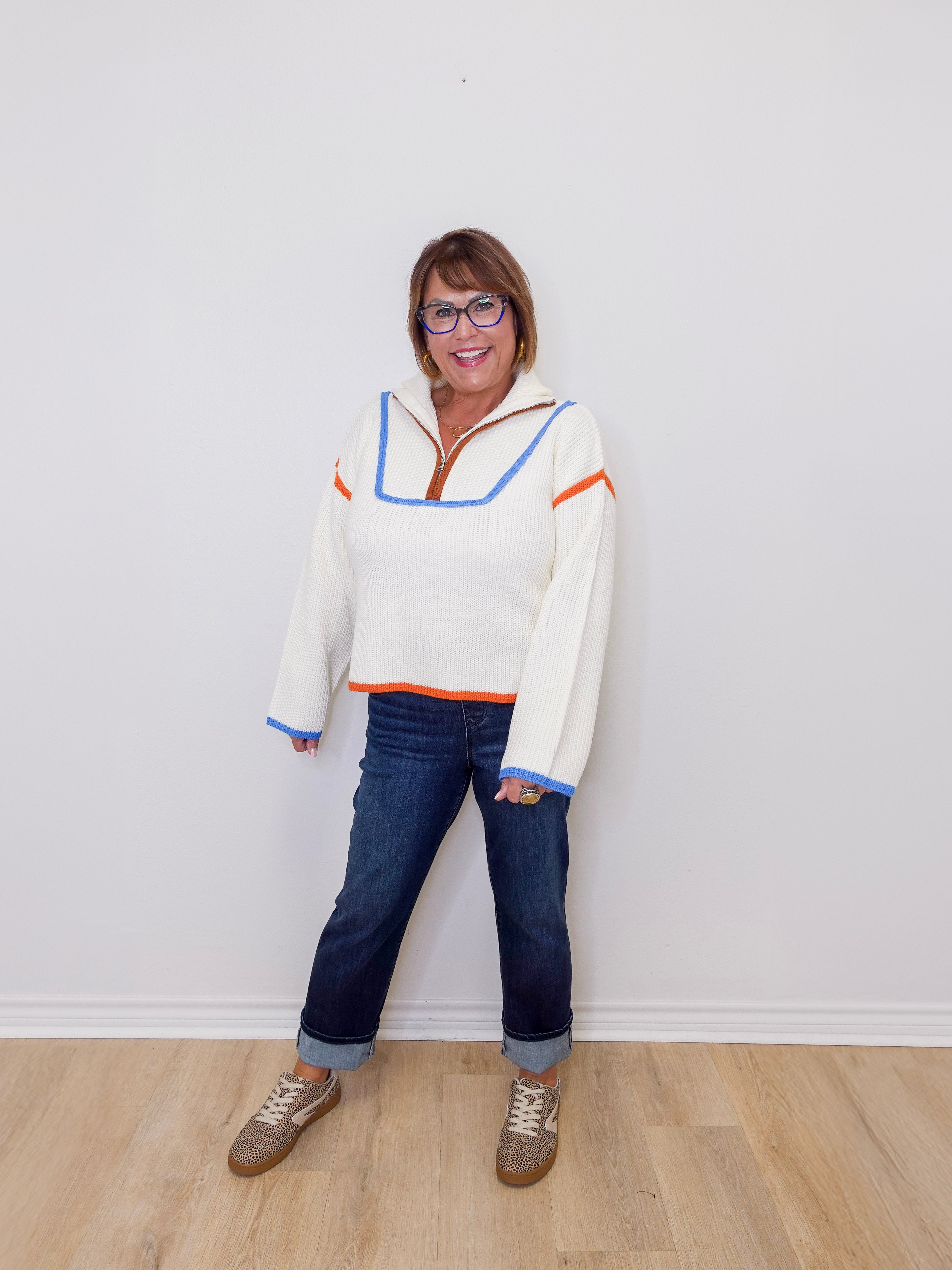 Person wearing a colorful sweater and jeans standing against a white wall.