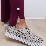 Person wearing leopard print slip-on shoes with a white sole on a wooden floor.