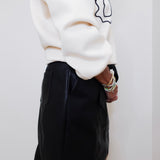 Person wearing a white sweater and black skirt against a white wall