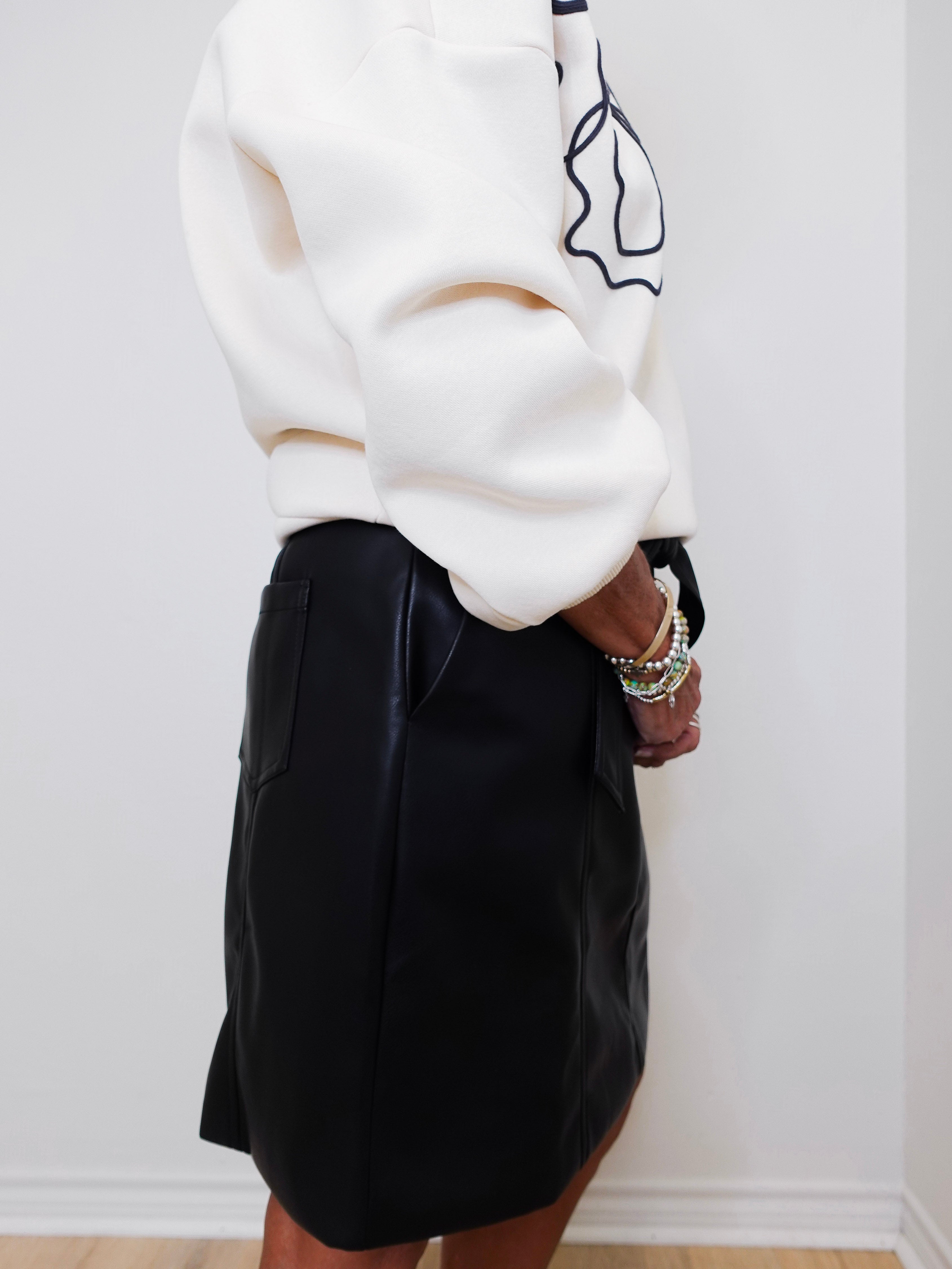 Person wearing a white sweater and black skirt against a white wall