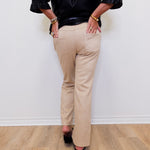 Person wearing a black top and beige pants against a white wall.