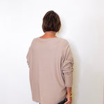 A woman wearing a v-neck jewel embellished sweater in front of a white wall.