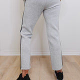 Person wearing gray jogger pants with black stripes on a light wooden floor.