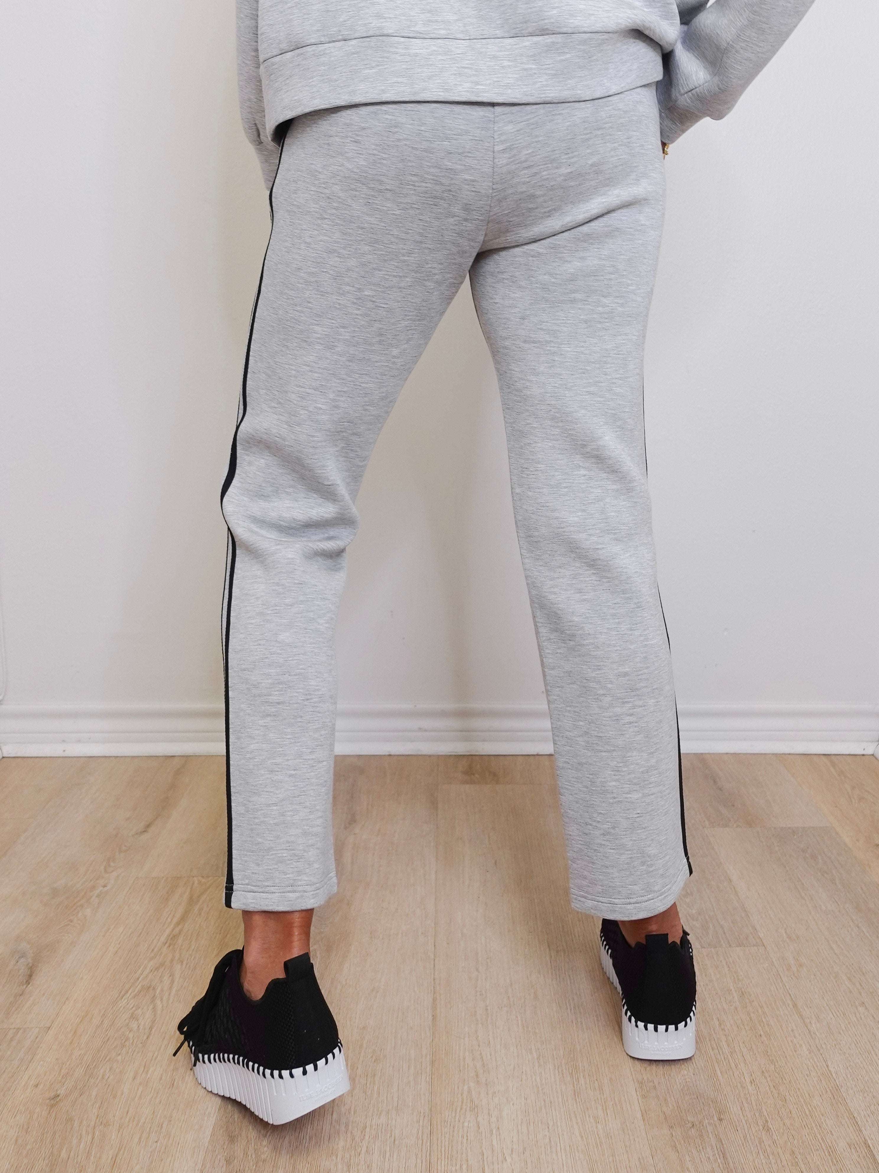 Person wearing gray jogger pants with black stripes on a light wooden floor.