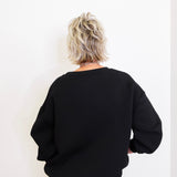 Person wearing a black sweater and blue jeans against a white background