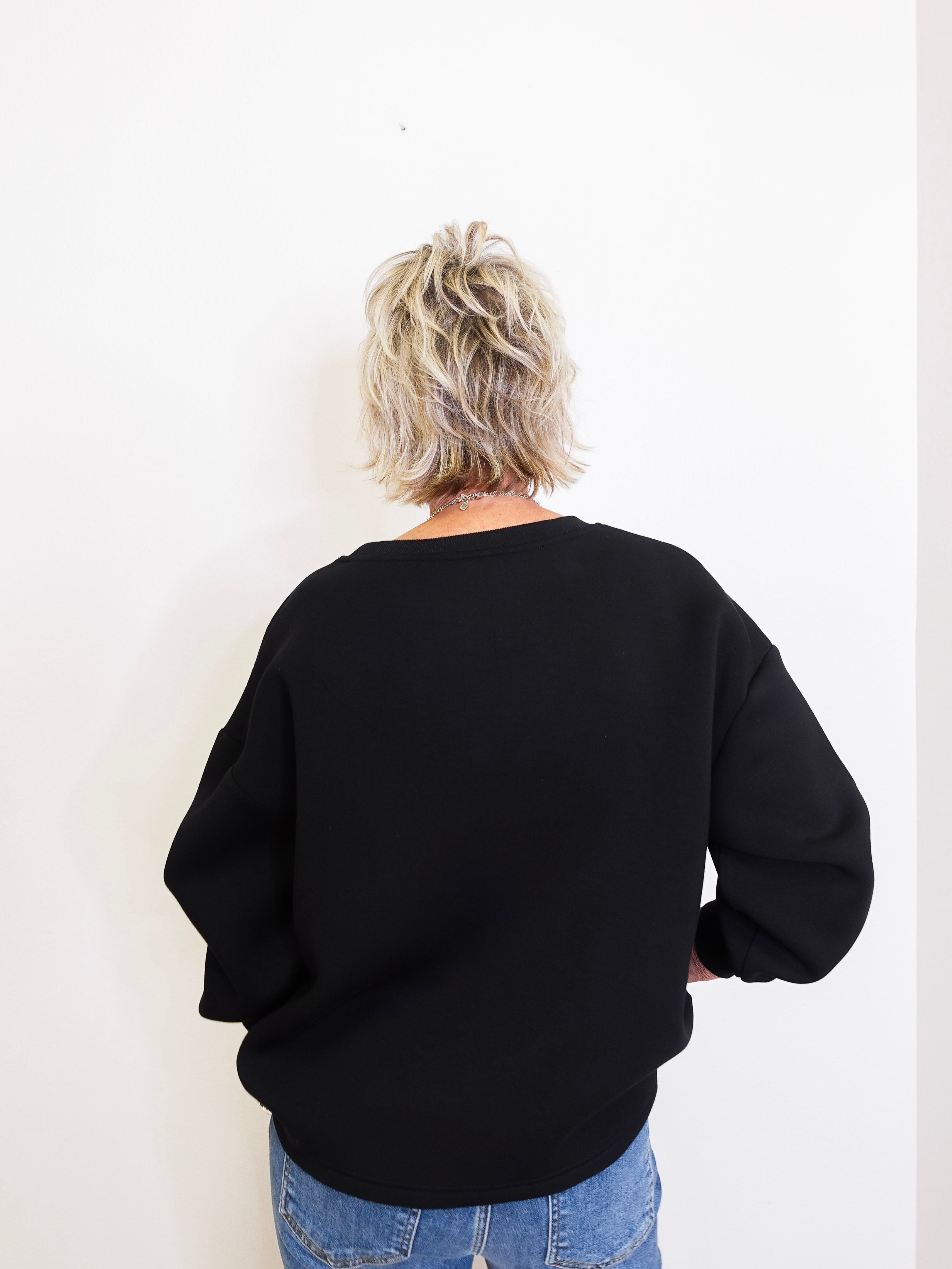 Person wearing a black sweater and blue jeans against a white background