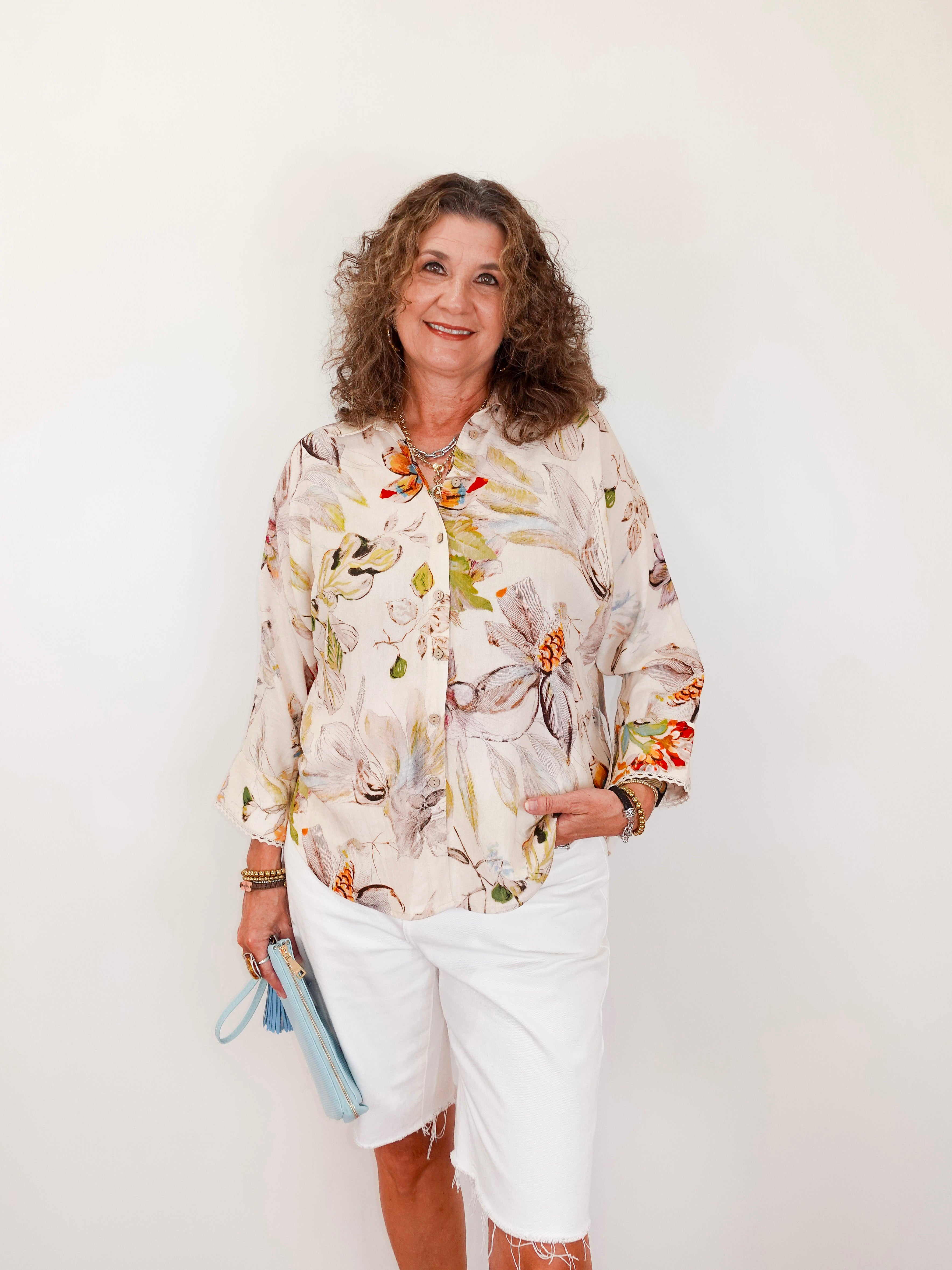 Woman wearing a floral blouse and white shorts against a plain background