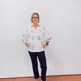 Person wearing a white floral blouse and dark pants against a plain background