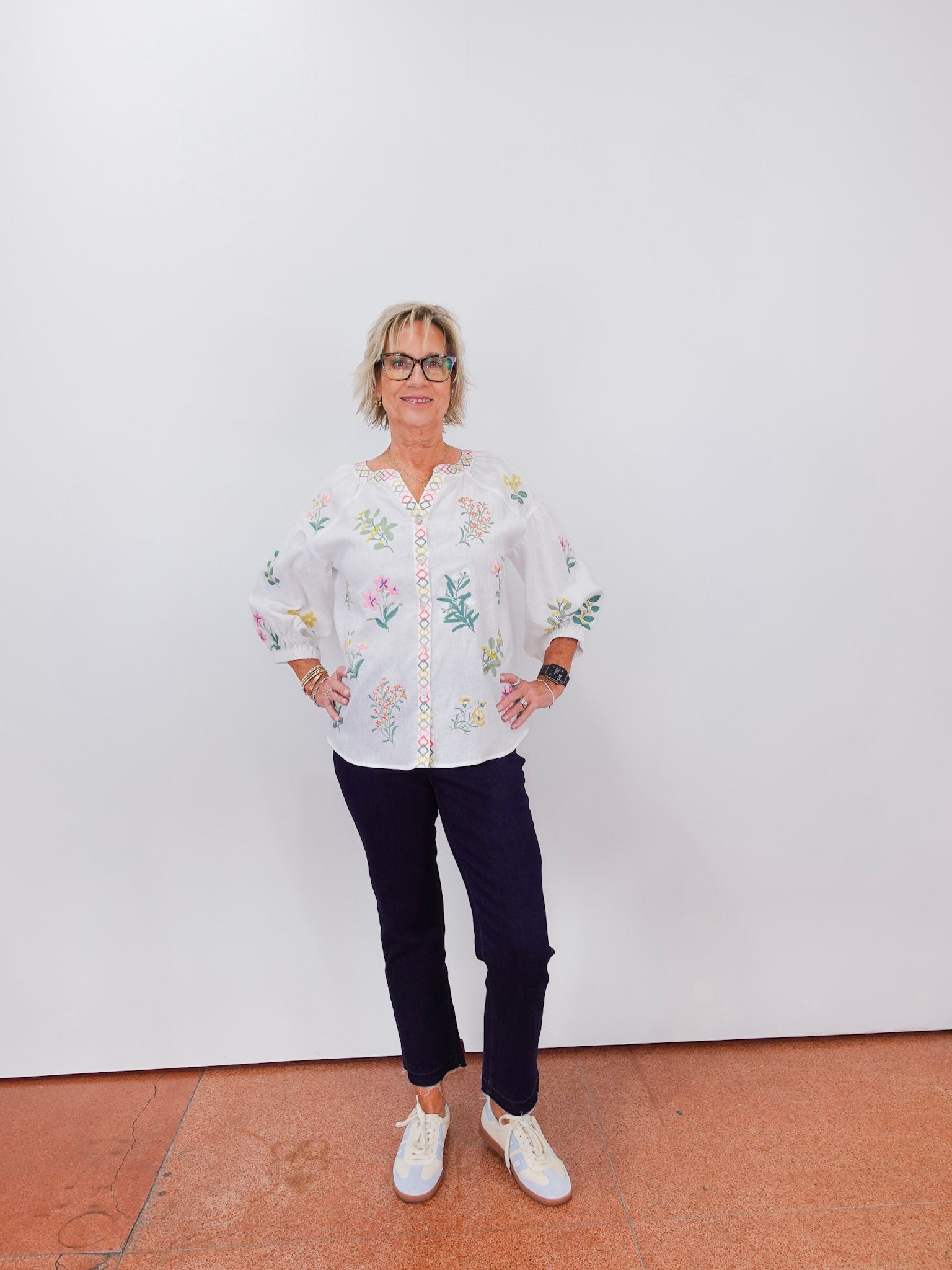 Person wearing a white floral blouse and dark pants against a plain background