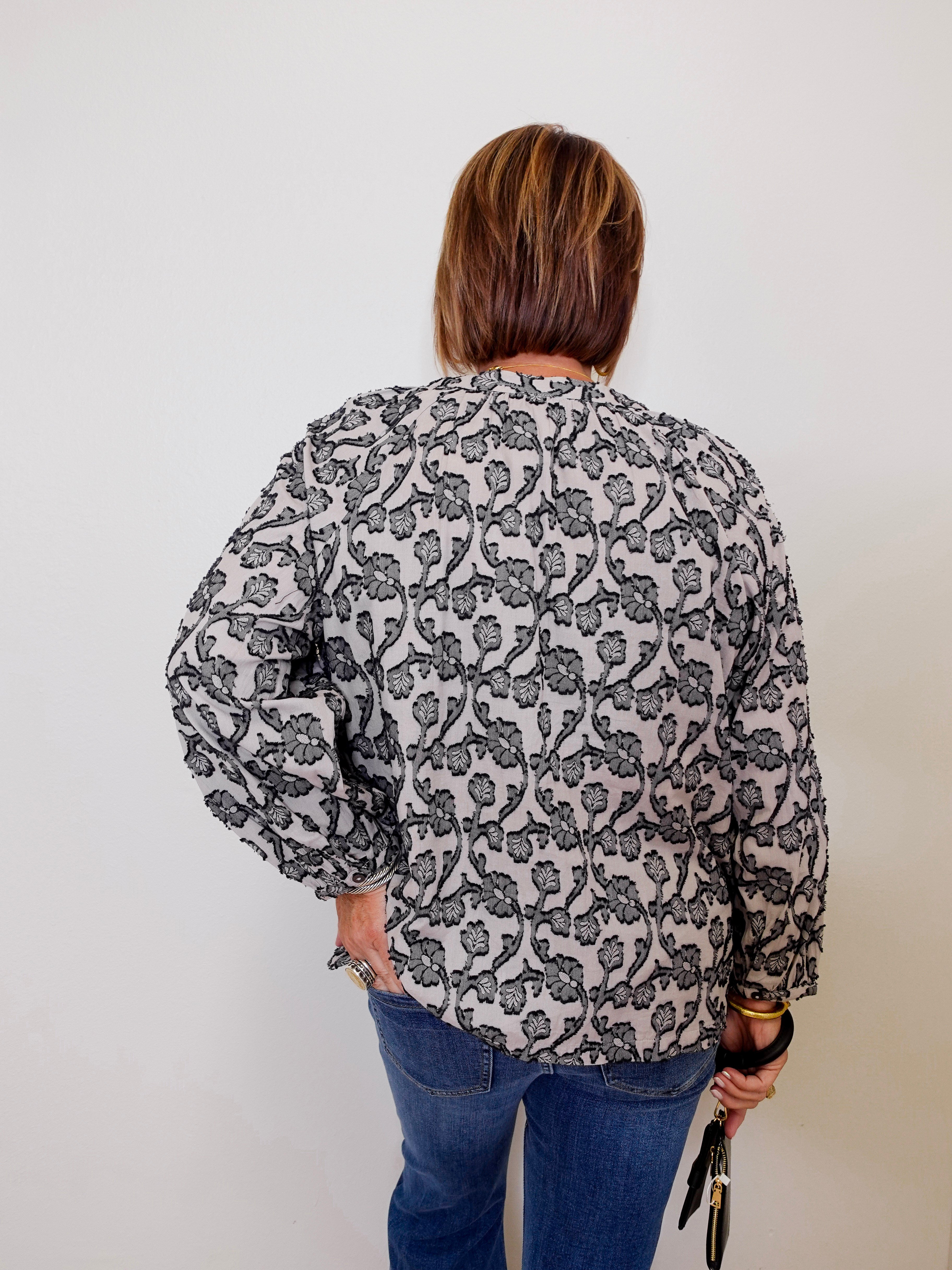 Person wearing a patterned blouse and jeans against a plain background