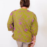Person wearing a green patterned blouse against a white background