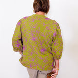 Person wearing a green patterned blouse against a white background