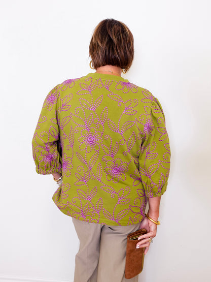 Person wearing a green patterned blouse against a white background