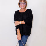 Woman wearing a black sweater and blue jeans, holding a patterned handbag against a white background