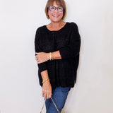 Woman wearing a black sweater and blue jeans, holding a patterned handbag against a white background