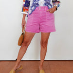 Person wearing a colorful embroidered top and pink shorts against a white background