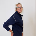 Woman wearing a navy blue jacket with white accents against a plain background