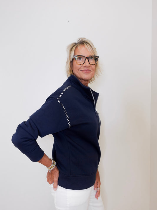 Woman wearing a navy blue jacket with white accents against a plain background