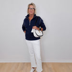 Person wearing a navy blue jacket, white pants, and white sneakers against a plain white wall.