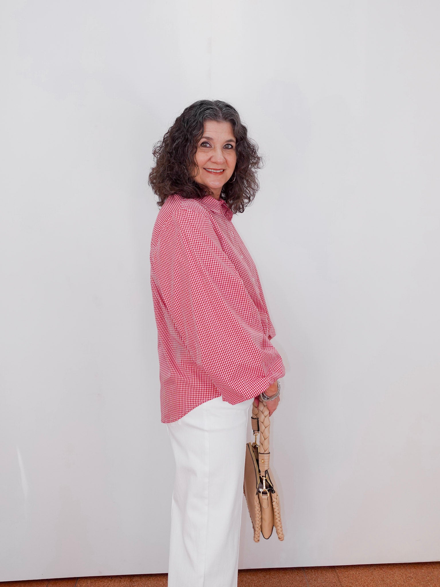 Woman wearing a red checkered shirt and white pants against a plain background