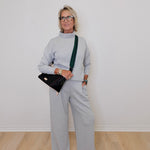Woman wearing a gray outfit with a black handbag against a white wall.