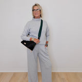 Woman wearing a gray outfit with a black handbag against a white wall.