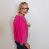 Person wearing a bright pink sweater and dark jeans against a plain background