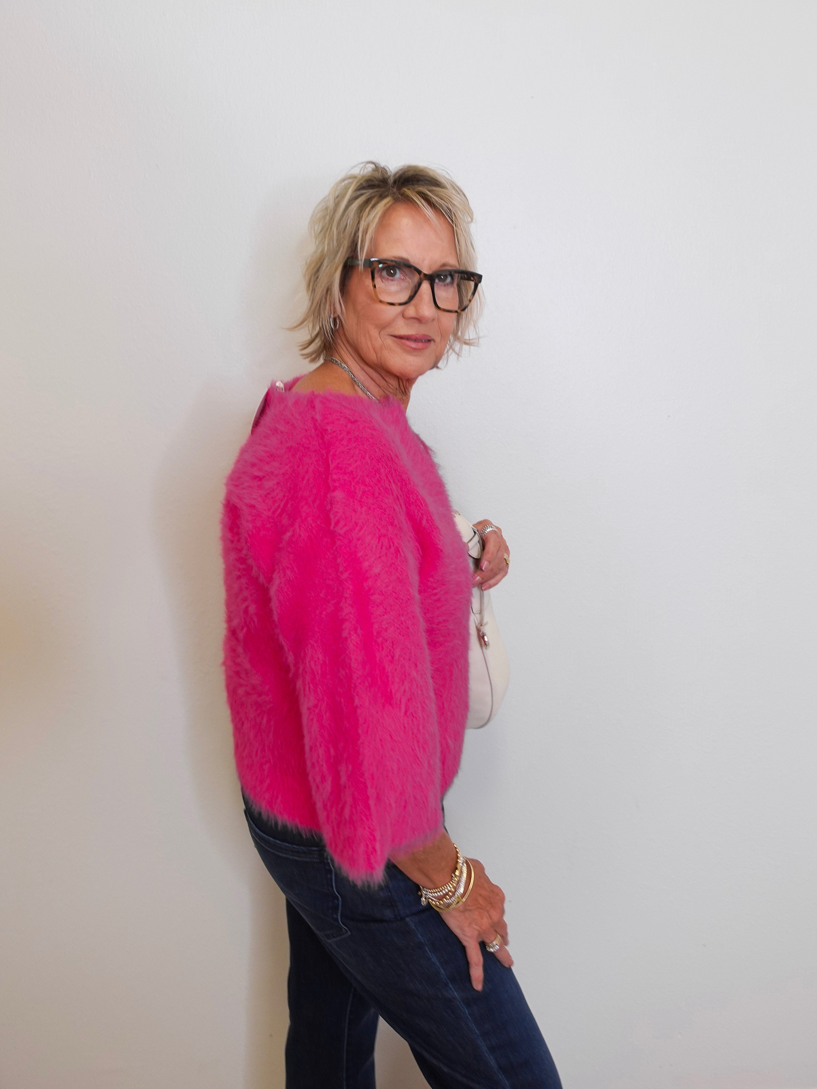 Person wearing a bright pink sweater and dark jeans against a plain background