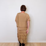 Person wearing a beige layered dress against a white wall.