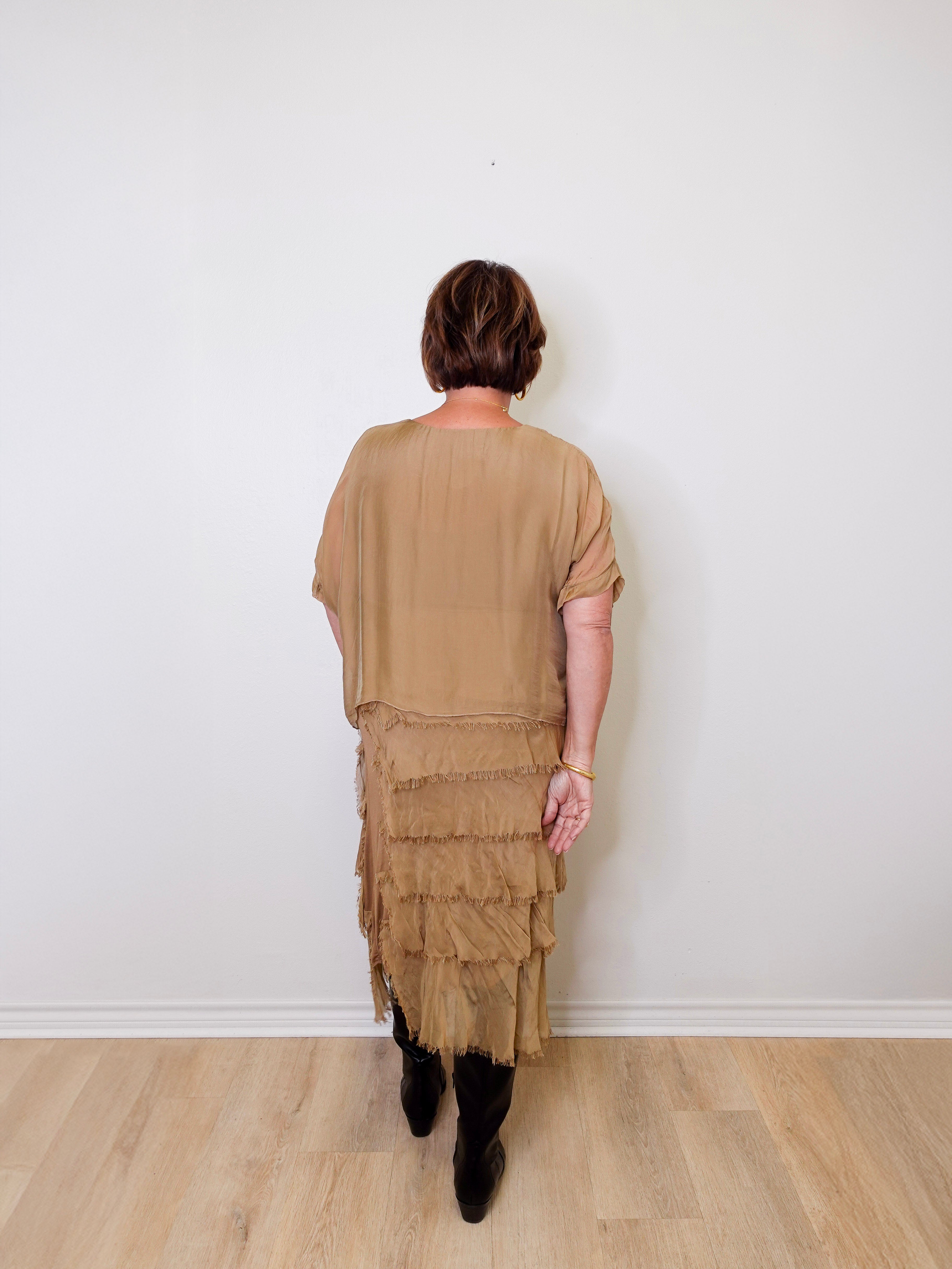 Person wearing a beige layered dress against a white wall.