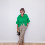 Woman wearing a green shirt and beige pants against a white wall.