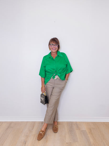 Woman wearing a green shirt and beige pants against a white wall.