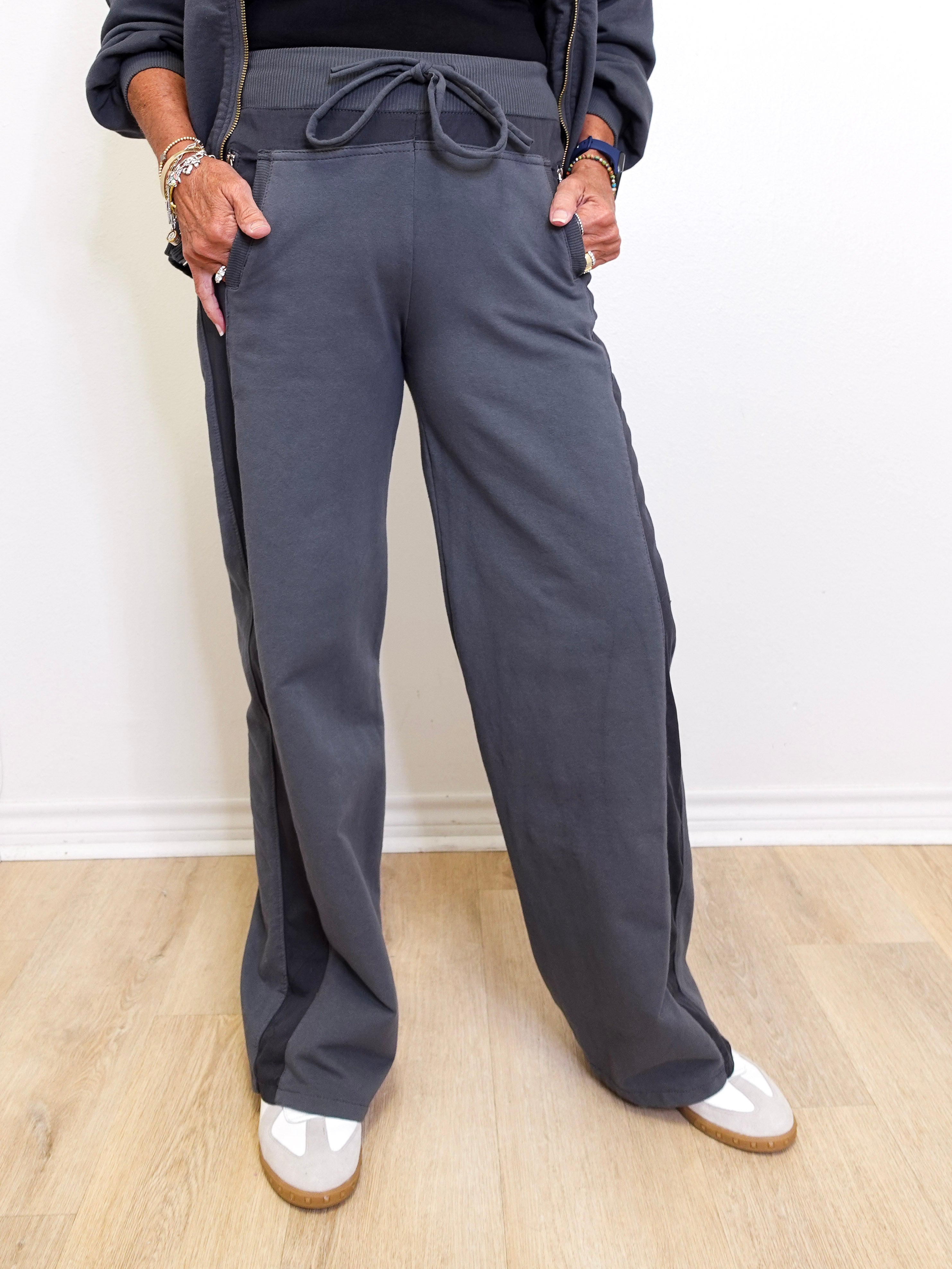 Person wearing gray sweatpants on a light wooden floor with a white wall background