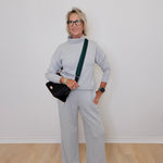 Person wearing a gray outfit with a black bag against a white wall