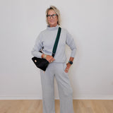 Person wearing a gray outfit with a black bag against a white wall